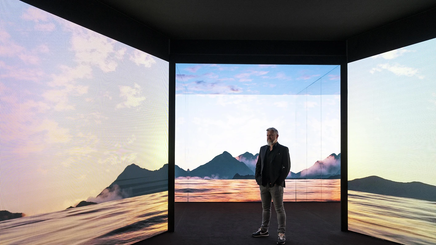 Person standing in front of a natural landscape video and a three-sided media wall.