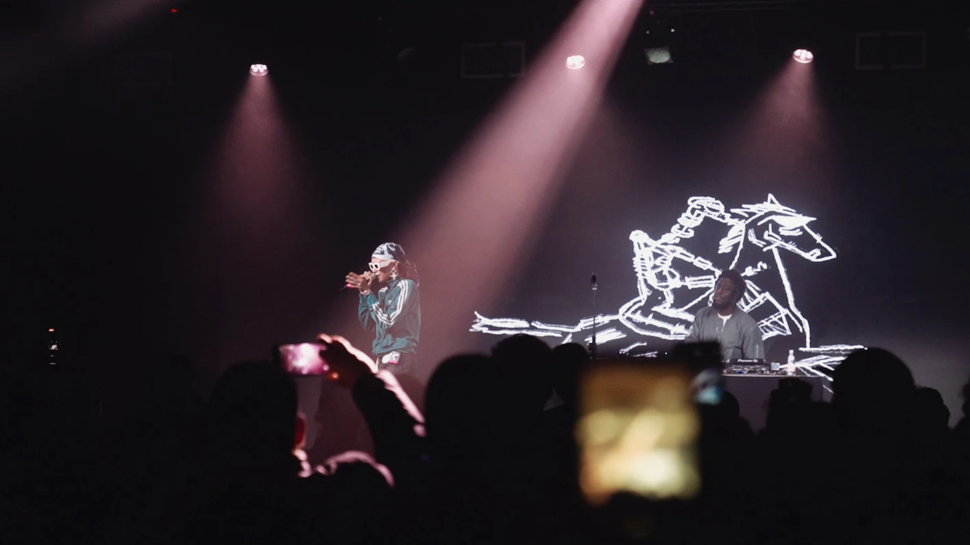 Artist performing under stage video and lighting with audience.