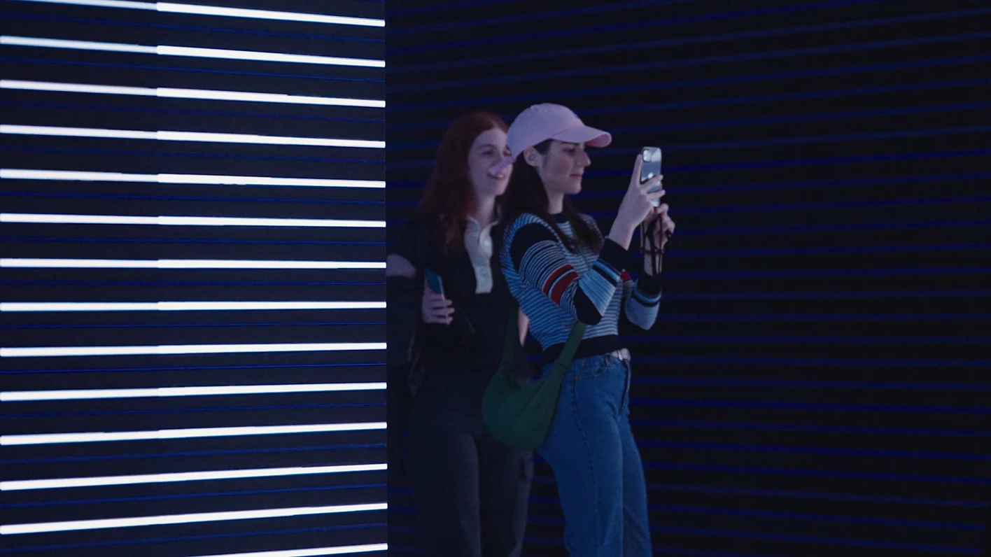 Visitor taking a photo in front of horizontal lighting patterns.