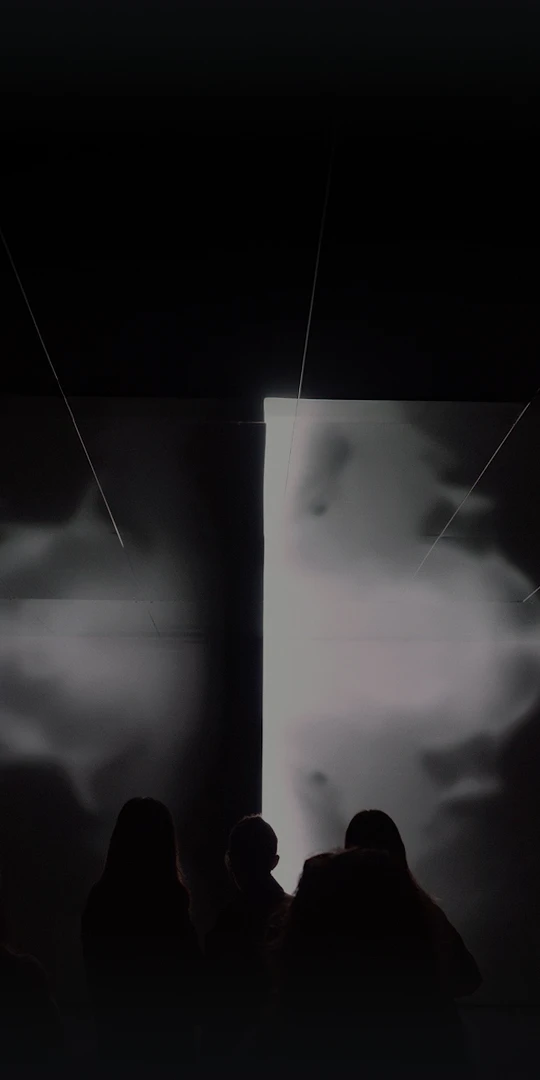 Bright media screen with silhouetted visitors in front.