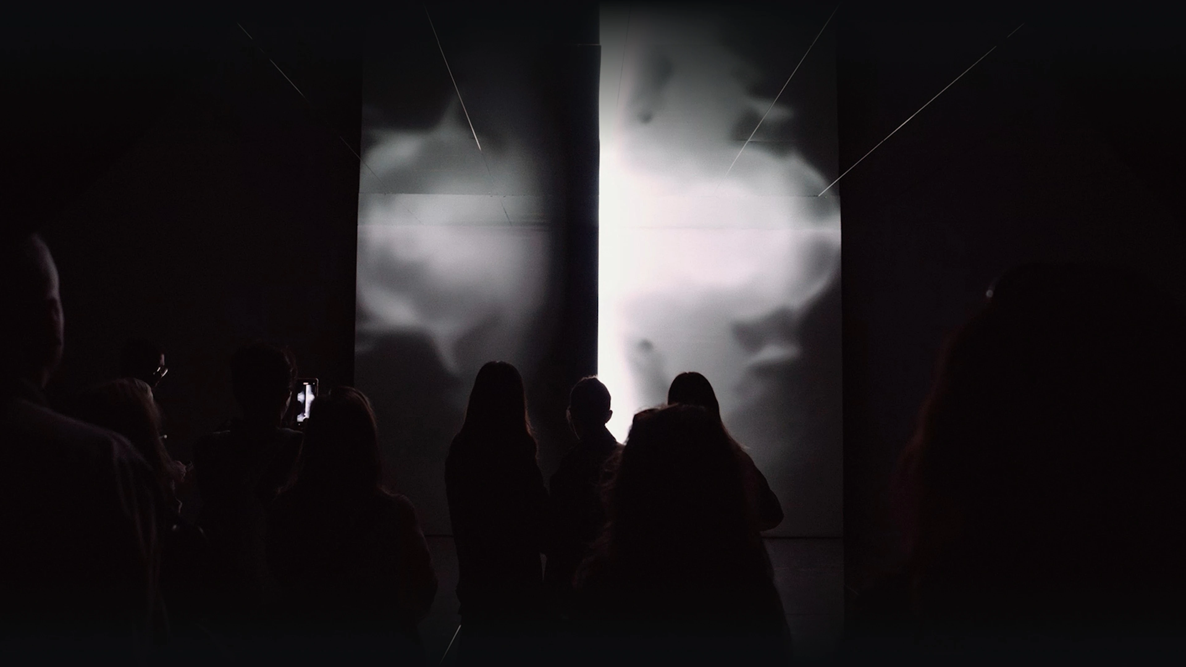 Bright media screen with silhouetted visitors in front.