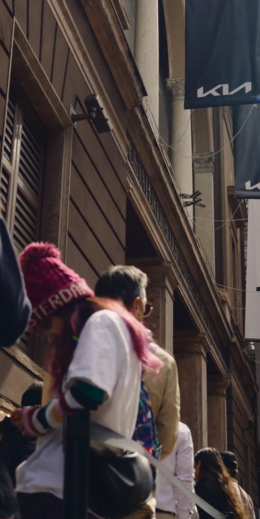 Kia logo flag on a building exterior and people walking along the street.