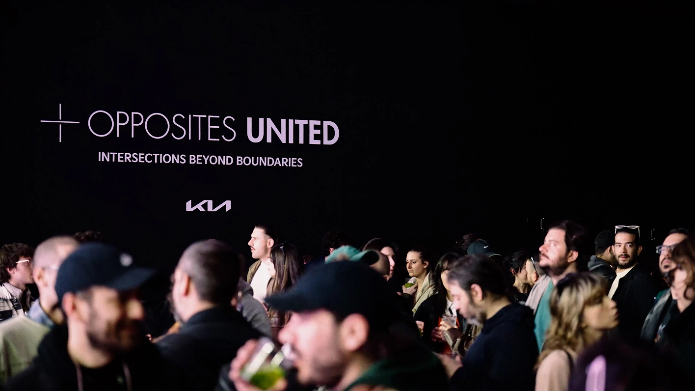 Exhibition hall with the typography ‘OPPOSITES UNITED’ and gathered visitors.