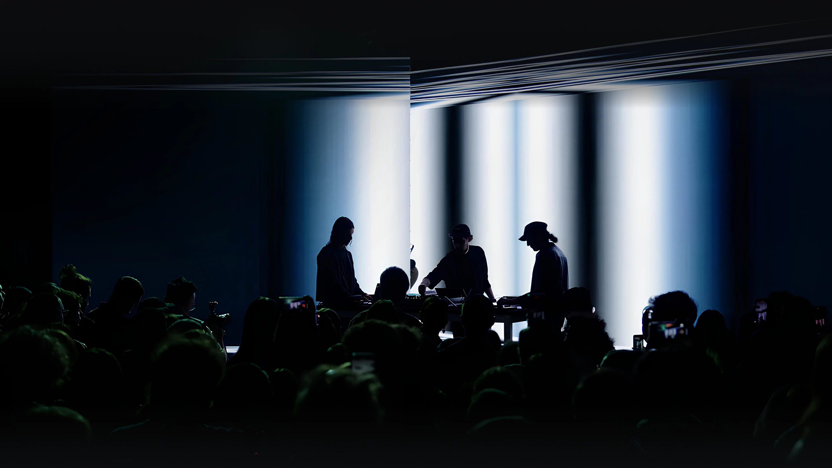 Three artists and audience silhouettes on a brightly lit stage.