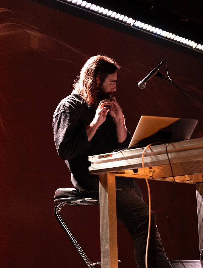 Artist Panamos performing at a table with a laptop and musical instruments.