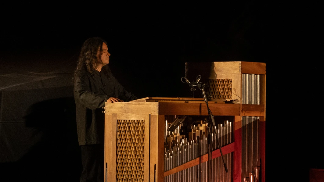 Musician playing a large pipe organ on a dark stage.