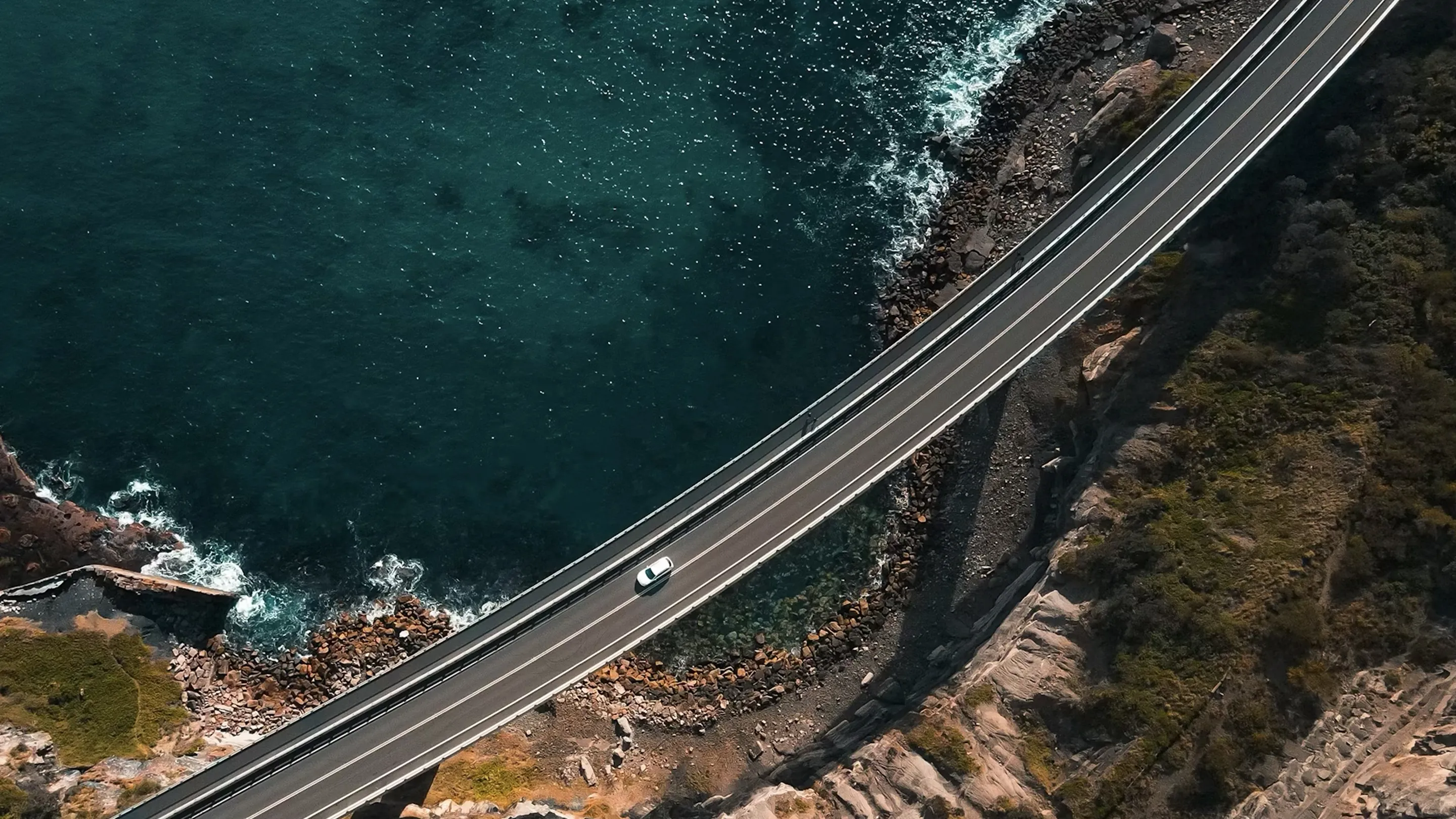 절벽과 바다 사이를 가로지르는 해안 도로 위 차량 주행 항공 촬영 장면