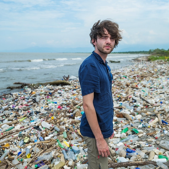 A man standing on a beach covered with plastic waste, with the ocean behind him