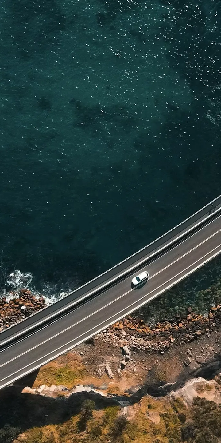 절벽과 바다 사이를 가로지르는 해안 도로 위 차량 주행 항공 촬영 장면