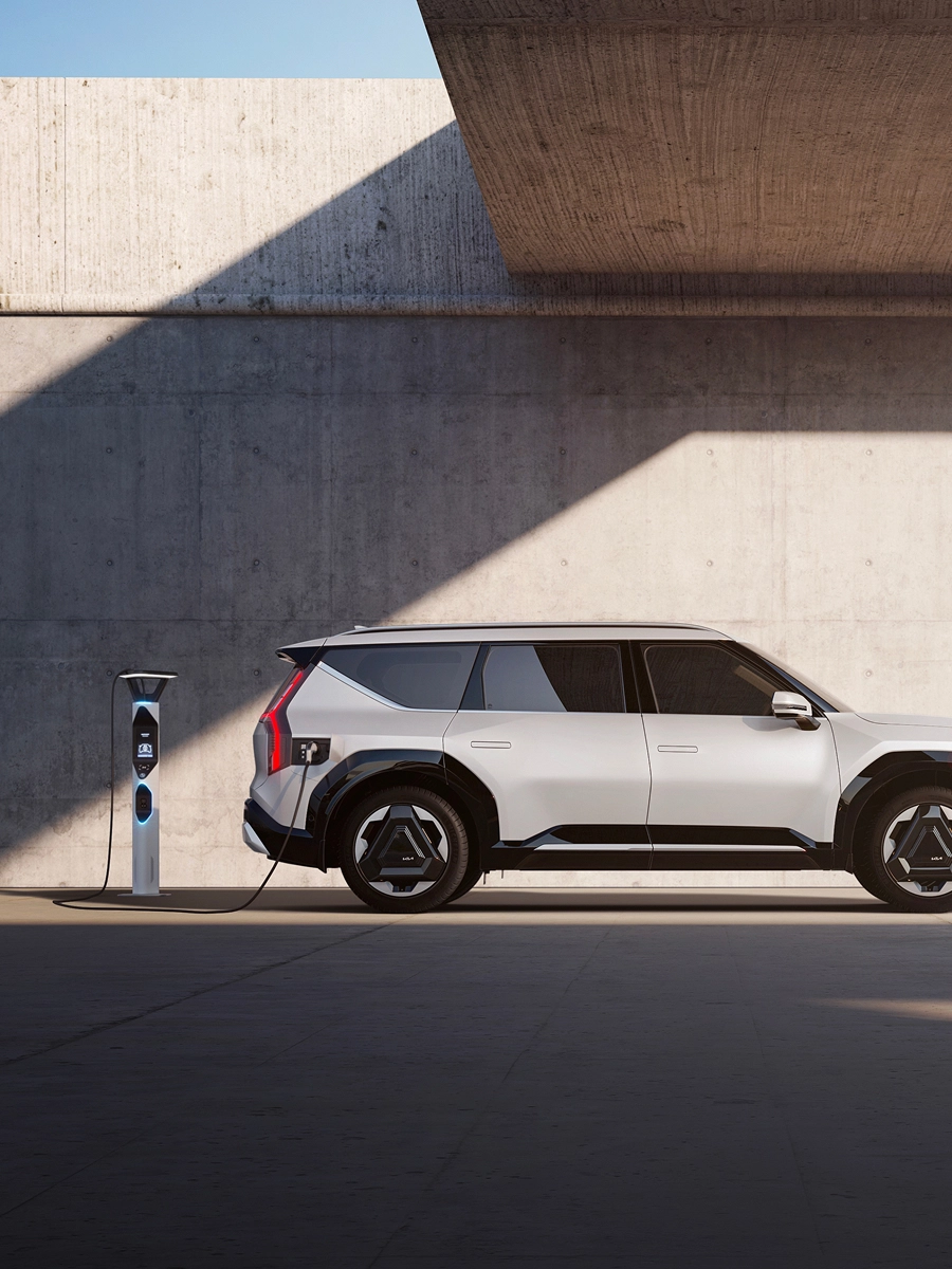 Side view of the Kia EV9 connected to a charging station in front of a modern architectural space