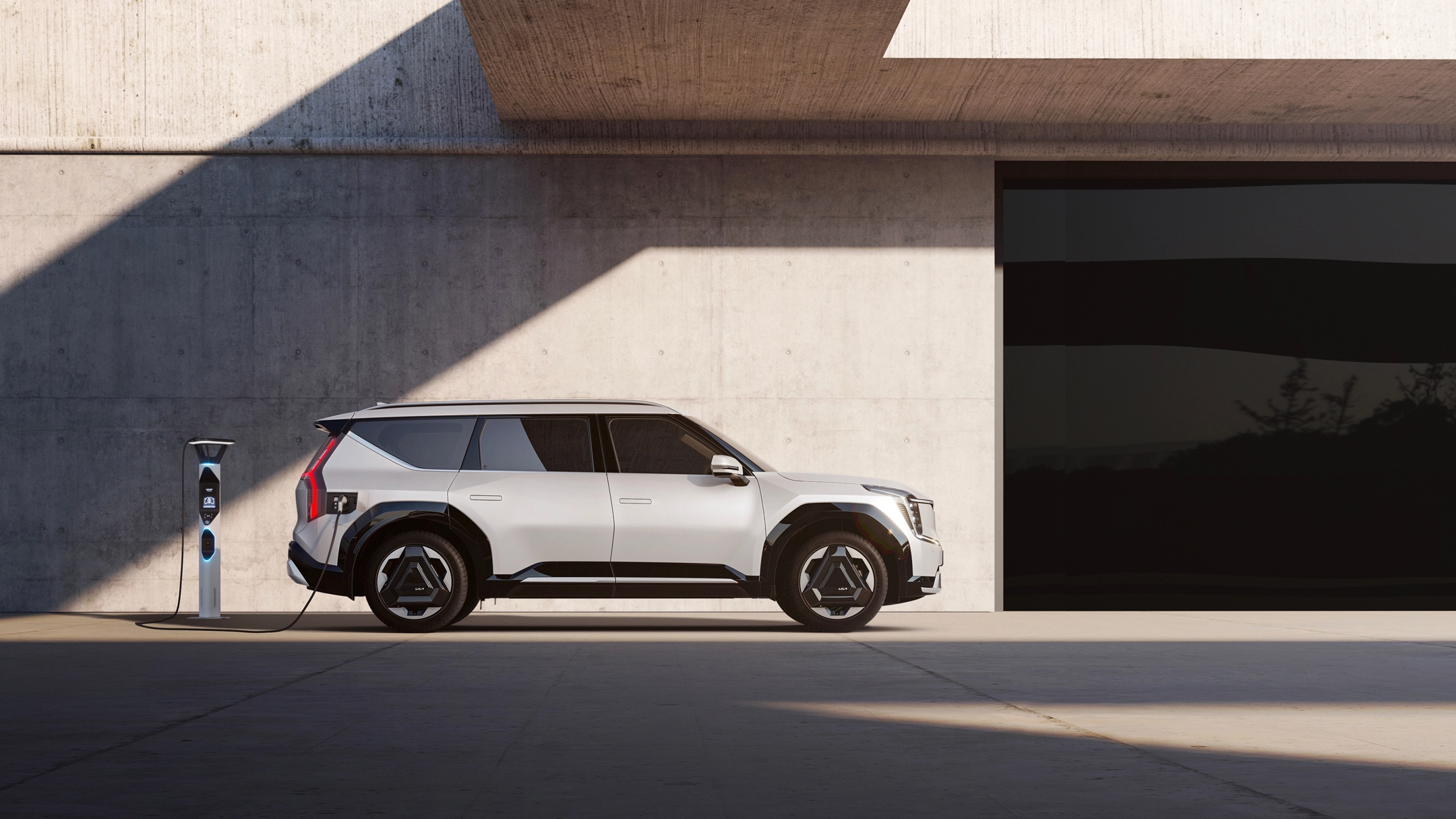 Side view of the Kia EV9 connected to a charging station in front of a modern architectural space