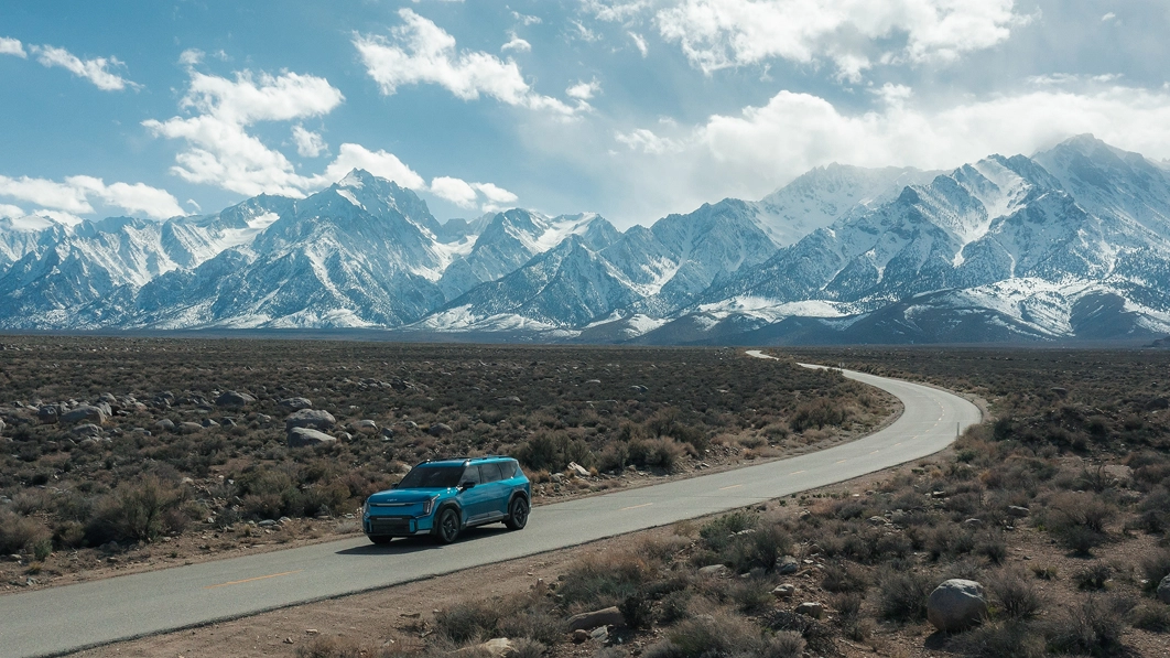 Kia EV9 driving along a winding road through a vast natural landscape