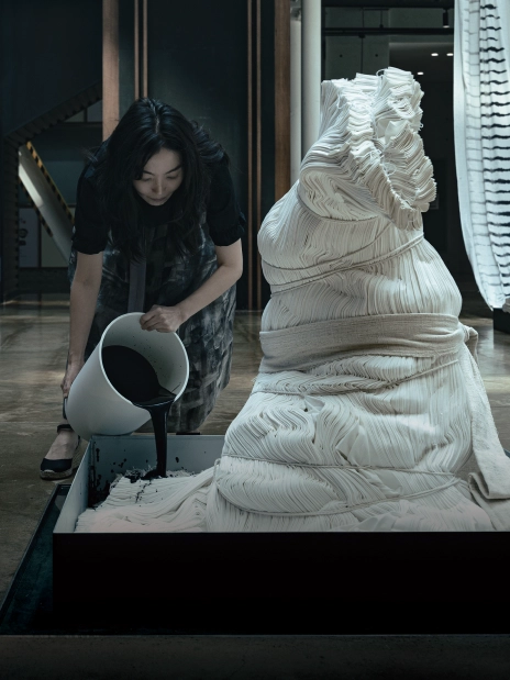 An artist pouring water onto a sculptural work