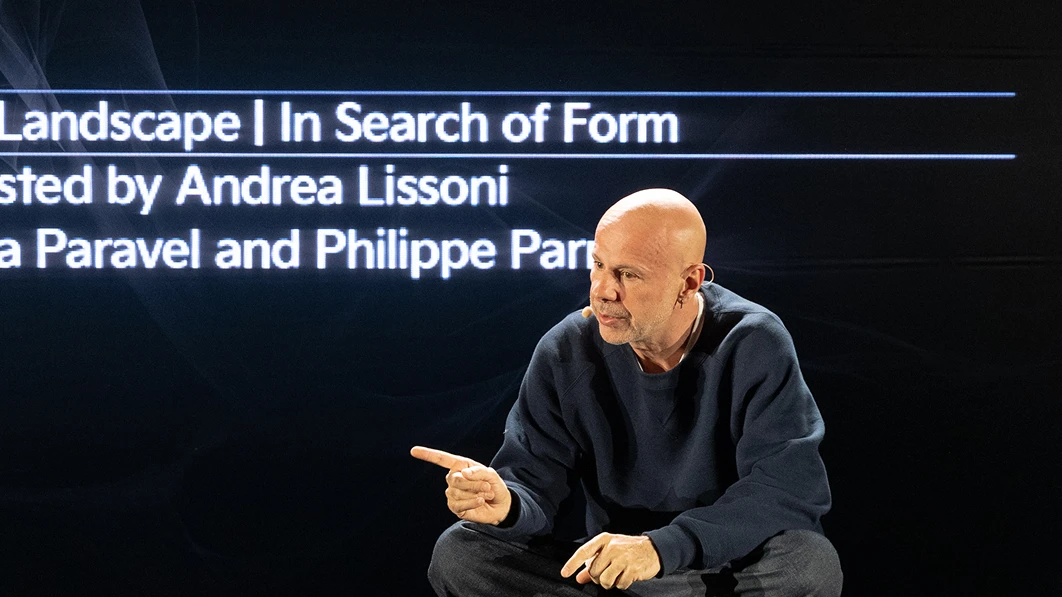 Curator Andrea Lissoni speaking in front of a screen displaying the exhibition title.