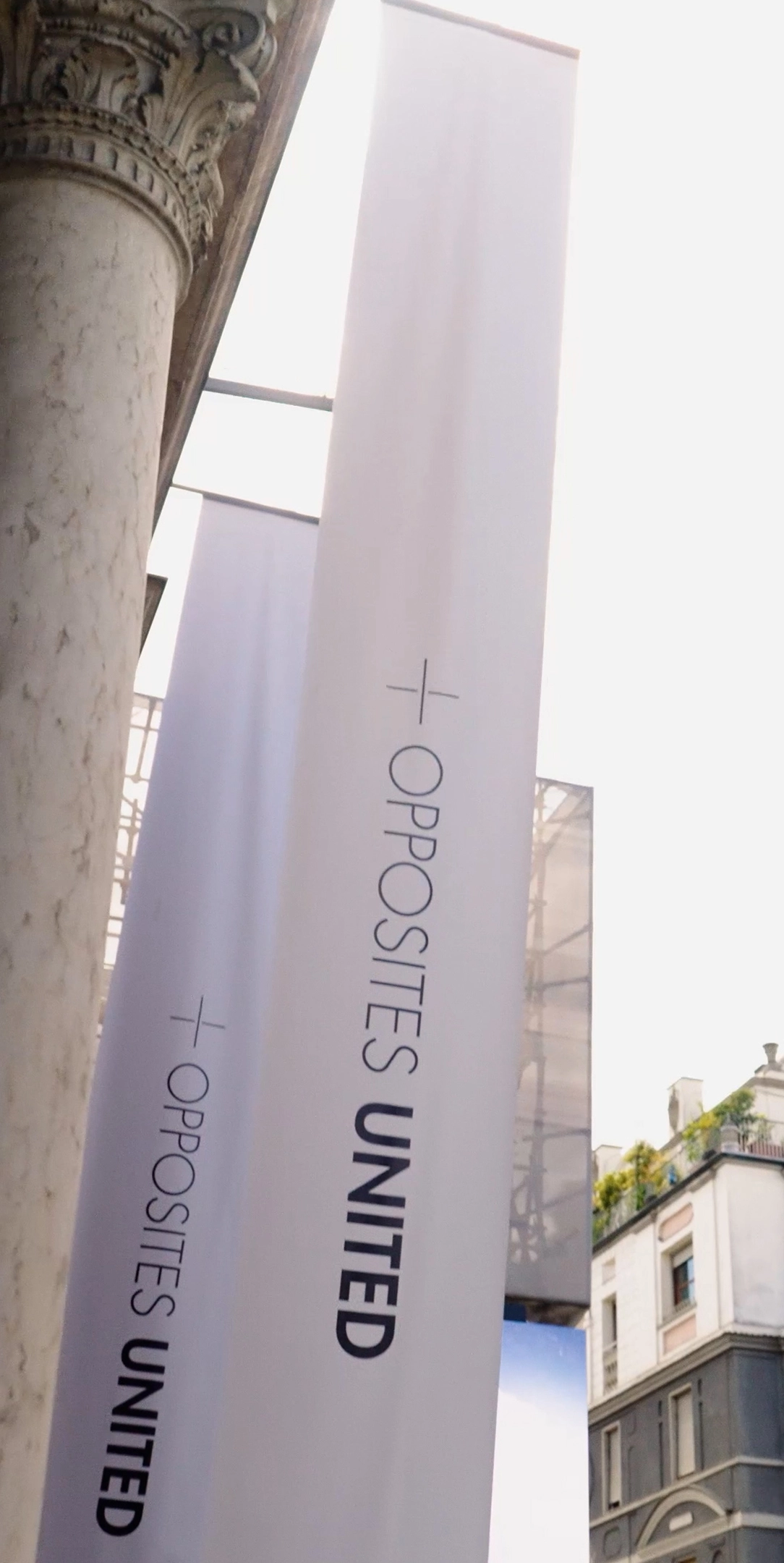 'OPPOSITES UNITED' 문구가 적힌 흰색 대형 현수막과 건물 기둥