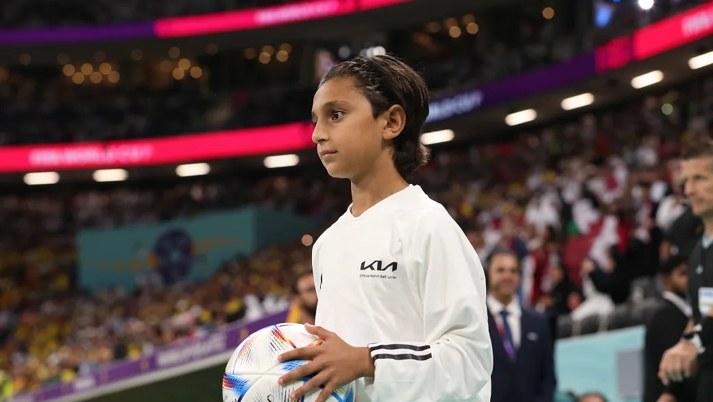 Ball kid entering the stadium holding a football while wearing a Kia-branded uniform