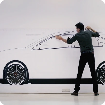 Person refining a side-view sketch of a Kia vehicle drawn on a wall