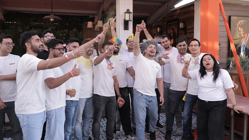 Kia India employees dressed in white raising both arms and cheering at the Holi festival