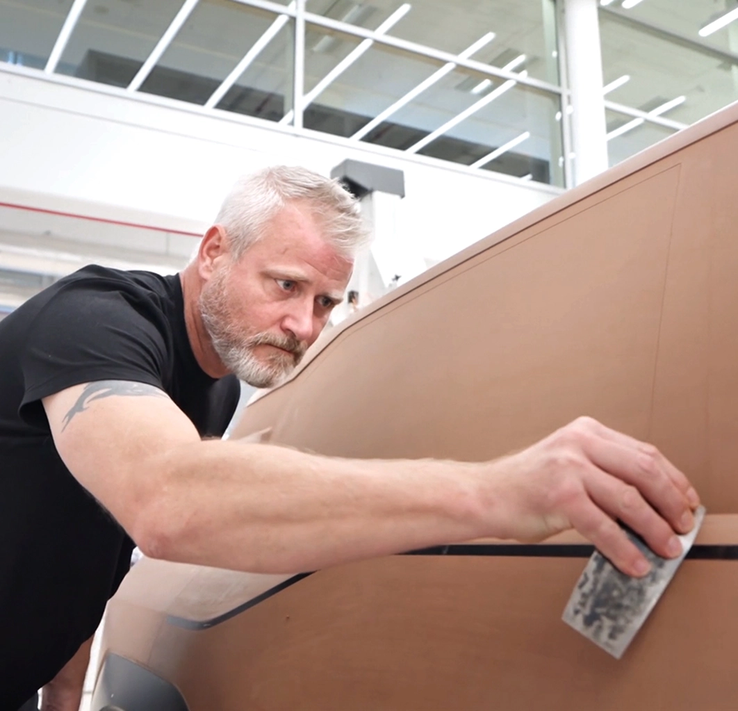 A clay modeler smoothing the curved surface of a full-size clay model with sandpaper in the Kia design studio