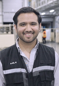 Kia Mexico employee Cesar smiling during an interview on the plant floor, wearing a KIA-branded work vest