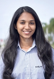 Kia India employee Sumadhu smiling during an outdoor interview, wearing a KIA-branded shirt
