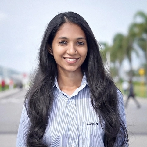 Kia India employee Sumadhu smiling during an outdoor interview, wearing a KIA-branded shirt