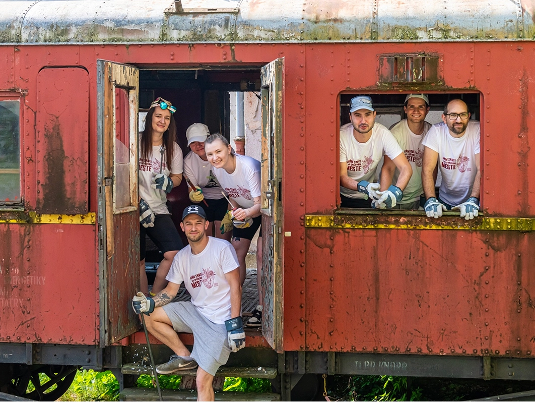 Kia Slovakia employees waving from inside a restored red vintage railway carriage during the 'Naše Mesto (Our City)' corporate volunteering campaign