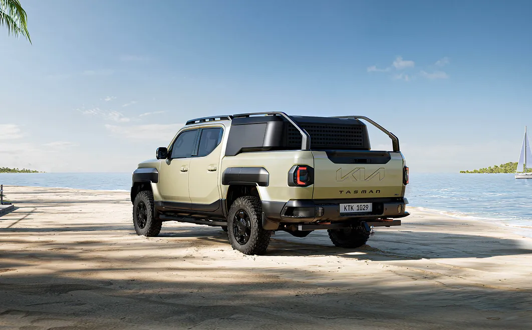 해안 풍경을 배경으로 한 기아 타스만 픽업트럭의 후면 사선 모습