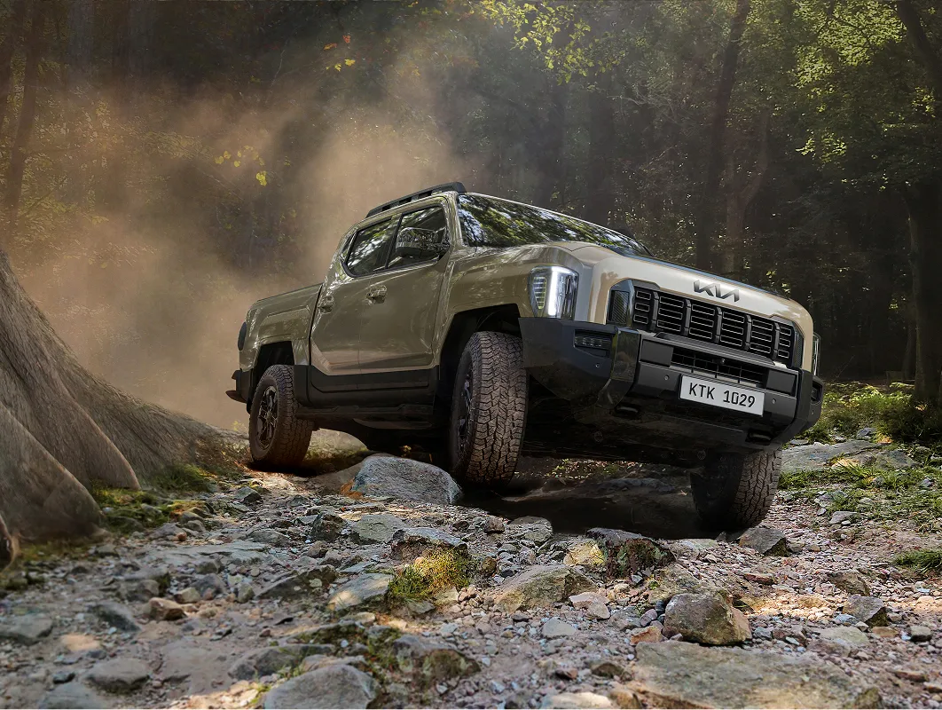 숲속 오프로드 지형을 주행 중인 기아 타스만 픽업트럭의 모습