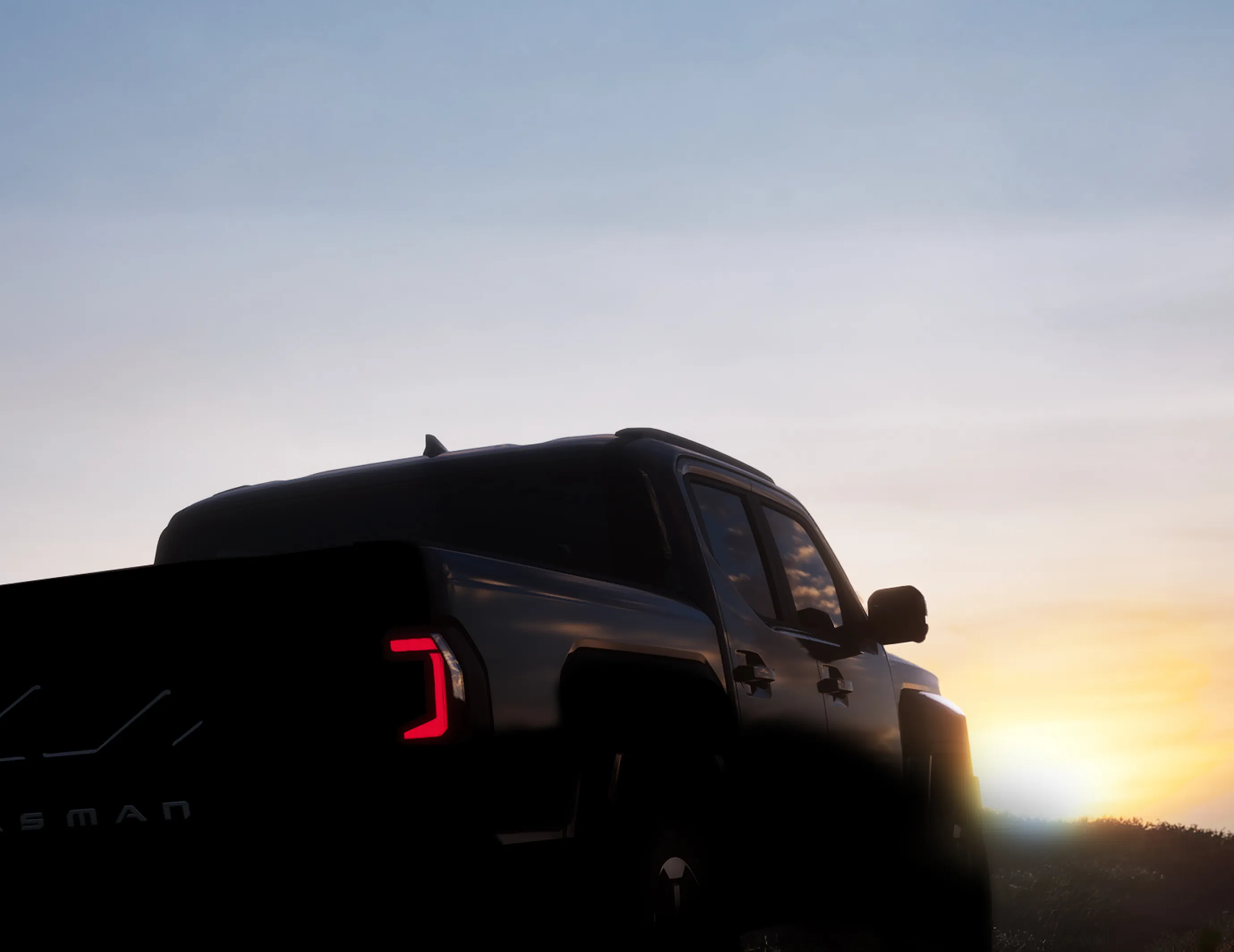 해 질 녘 실루엣으로 보이는 기아 타스만 픽업트럭의 후면 모습