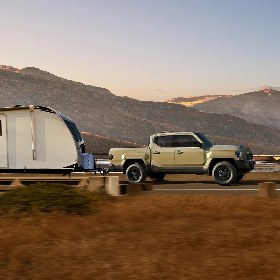 트레일러를 견인하며 자연 풍경 속을 주행하는 기아 타스만 픽업트럭의 모습