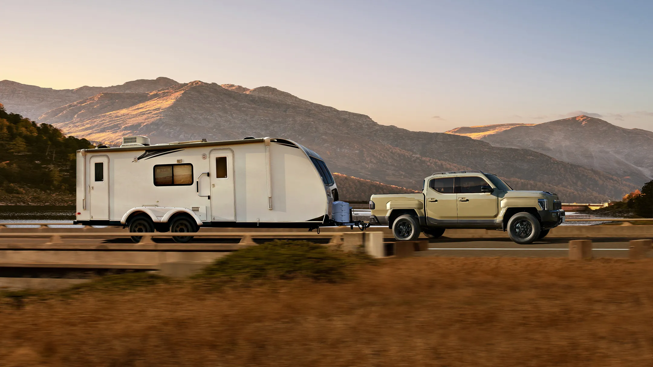 트레일러를 견인하며 자연 풍경 속을 주행하는 기아 타스만 픽업트럭의 모습